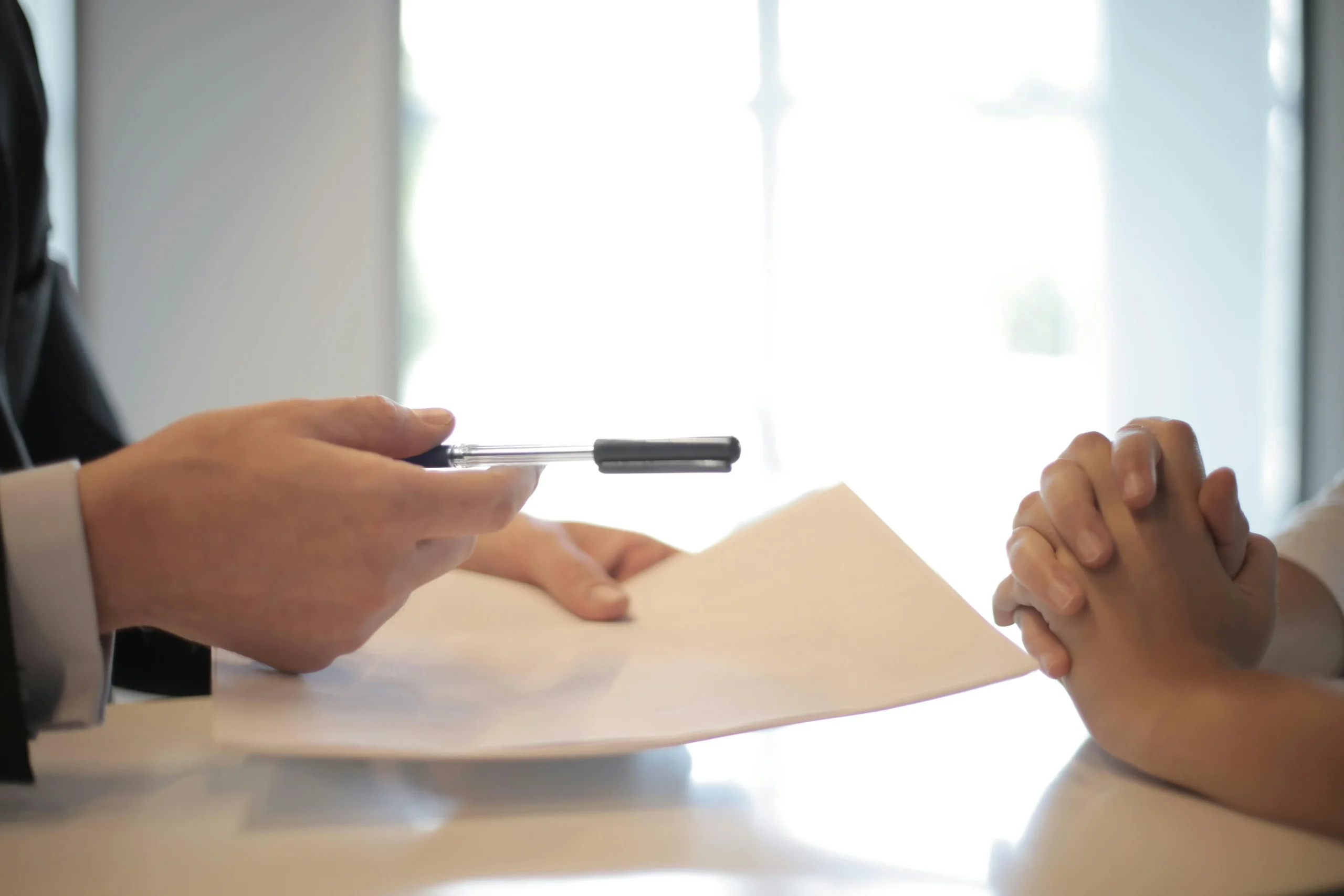 A banker holds a contract in one hand and a pen in the other and hands both to the customer for her to sign